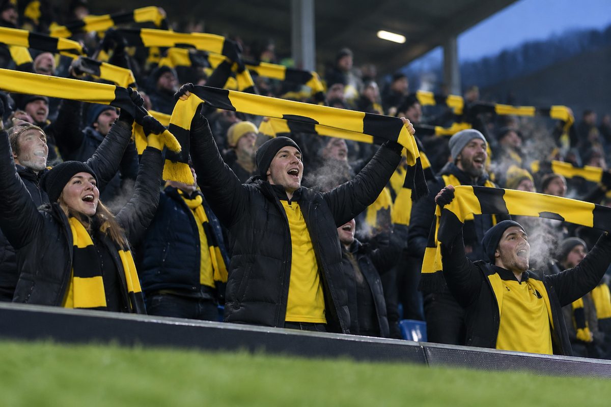 Supportere med skjerf på en tribune under en fotballkamp om kvelden